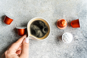 Hand holding cup of fresh espresso with capsules