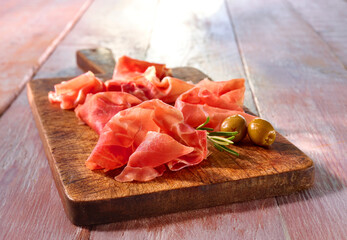 Serrano Schinken mit Oliven auf rustikalem Holzbrett