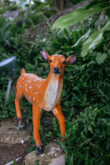 Close-up of painted deer statue standing among lush green foliage in Luhuitou Park on Hainan Island, Sanya.  Deer turning it's head scenic area.