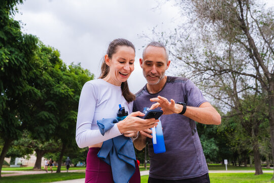 Two friends over forty checking health data on a smartphone after outdoor exercise
