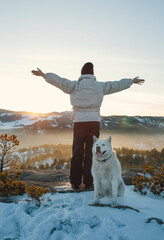 A woman stands on top of a mountain with a husky dog
