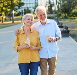 Happy active senior couple having fun talking drinking coffee and bonding in park outdoors