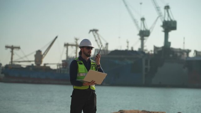 Worker inspects shipping area at port during daytime while using tablet for checks
