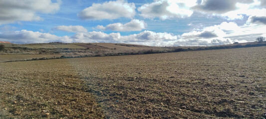 Campo de cultivo arado con colinas al fondo bajo cielo azul con nubes en Burgos, Espa&ntilde;a