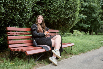 Young woman sitting on park bench with coffee cup on overcast day