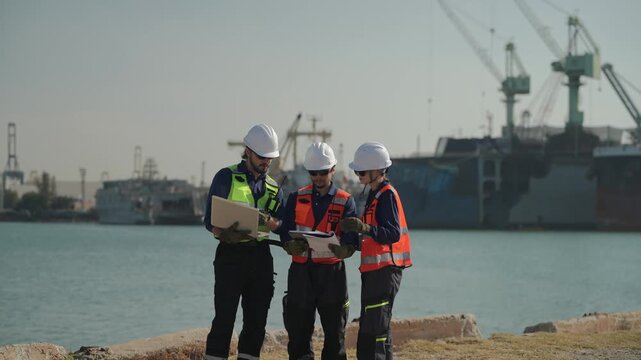 Workers discuss plans by the water at a busy port during the day