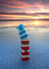 self created wooden lighthouse with knitted hat on the ice beach in winter