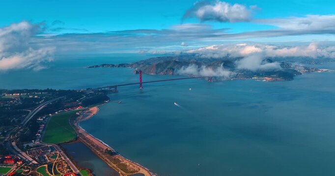 Boat moves by San Francisco Bay towards the Golden Gate Bridge. Clouds float in the sky over the scenery. California, USA.