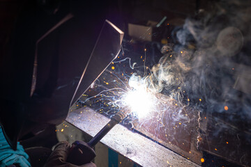 Welding old metal car part at workshop, sparks and smoke flying around, closeup detail