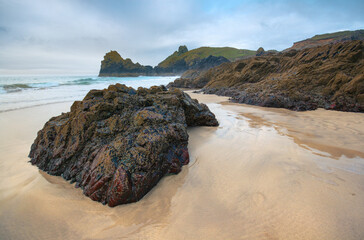 Large dark rocks on smooth sand beach at Kynance Cove, ocean in background