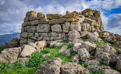 Prehistoric nuraghe stone structure rising from green landscape under dramatic sky in Sardinia