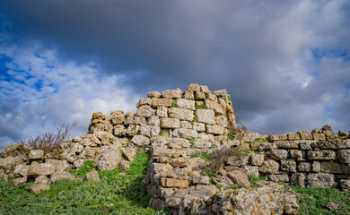 Prehistoric nuraghe stone structure rising from green landscape under dramatic sky in Sardinia