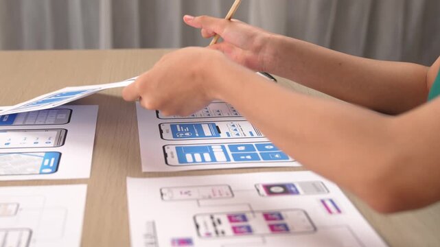 Startup company employee planning for user interface prototype for mobile application or website in office with model of program on desk. UX UI designer consider user friendly interface plan. Synergic