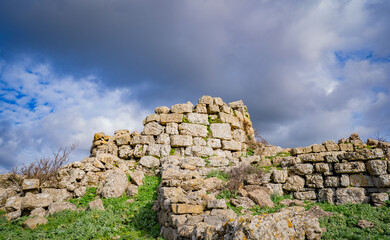 Prehistoric nuraghe stone structure rising from green landscape under dramatic sky in Sardinia
