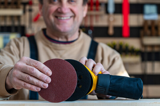 Male carpenter in a carpentry workshop fixing an sandpaper on a orbital wood sander for wood floor renovation, closeup. Seasonal house chores, woodworking, restoration