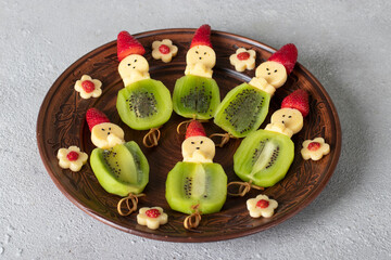 Canape with cheese, kiwi, and strawberries shaped like people on brown plate