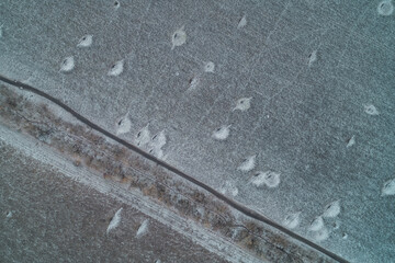 Aerial top down view of asphalt road cutting through damaged frozen fields with crater patterns resembling lunar landscape or war zone aftermath