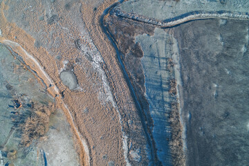Textured frozen wetland landscape with dry orange reeds and long tree shadows featuring winter frost details aerial top down view