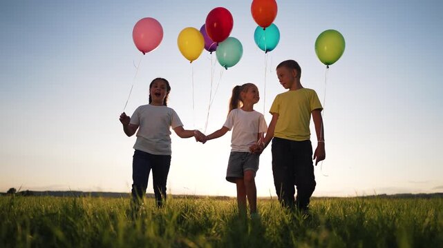 Children walk holding colorful balloon strings across green grass field at sunset smiling and laughing child kid showing friendship and family bond outdoor play energy and joy carefree child
