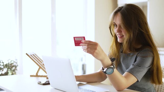 Woman shopping online with credit card smiling while using laptop to make internet purchase entering payment details for ecommerce order casual home setting with relaxed posture and focused expression