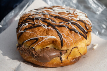 A generously filled round donut pastry brimming with chocolate cream and topped with white and dark icing in Bansko, Bulgaria