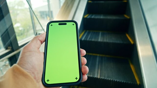Footage Of Unrecognizable Caucasian Young Man Holding Smartphone With Green Screen While Standing On Escalator Indoors. Mobile Phone Mockup For App Interface And Copy Space.