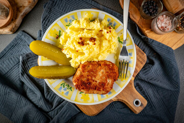 Minced meat cutlet served with mashed potatoes and pickled cucumber.