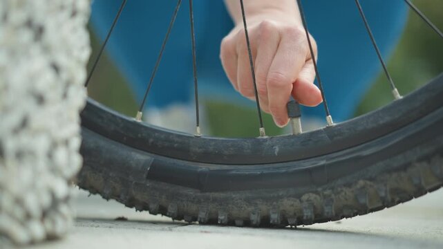 closeup mountain bike tire hand extracting nail lodged in chunky tread riders hand grips metal shaft and pulls nail beside blue jacket gritty pavement and grass hints quick roadside remedy
