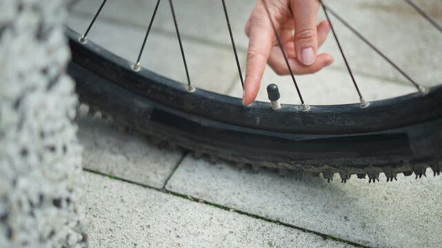 closeup bicycle valve cap removal by womans fingers, stone sidewalk, deflated tire rim, fingertip lifting cap and core, focused quick motion, ready to inflate and continue commute, tense to relieved