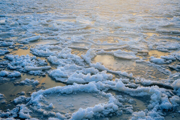 Obraz premium Close-up view of broken ice sheets floating on a cold body of water during winter. The fragmented ice pieces create natural patterns and textures, while soft sunlight reflects on the surface, adding a