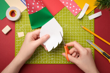 Making a gnome craft. Hands cut out a beard from white paper. Creative process.