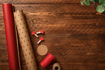 Gift wrapping background with supplies on wooden table with craft paper rolls, scissors, twine and tag. Valentine copy space.