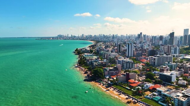 Aerial view of Jo&atilde;o Pessoa coastline in Para&iacute;ba, Brazil, showing turquoise ocean, urban skyline, sandy beaches, and tropical city landscape under clear blue sky.