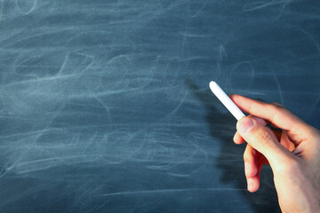 Hand holding chalk against blackboard with copy space. Education and school concept