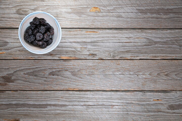 Dried Plums in Handmade Porcelain Bowl on Wood Background
