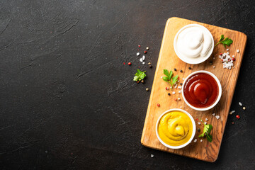 Ketchup, mayonnaise and mustard in the bowls on black background.