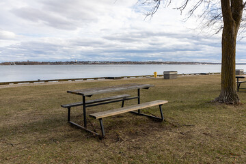Wooden picnic table in riverside park under cloudy sky in early spring.