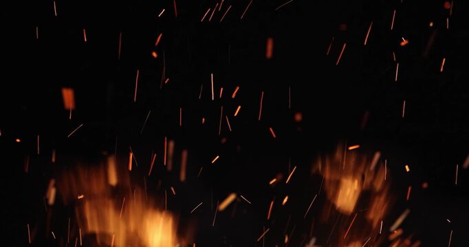 Fire and sparks at night close-up, slow motion. The flames of burning wood log fire on black background. Glowing sparks rising from burning firewood at night