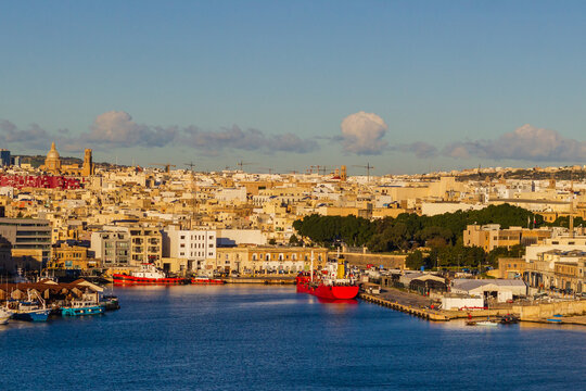 Golden Hour Waterfront Of A Mediterranean Port City With Historic Buildings And Red Boats