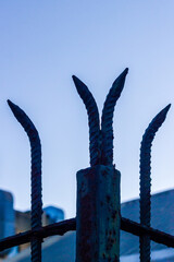 Rusty Iron Fence Spikes Silhouette Against a Clear Blue Sky at Dusk