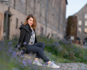 Stylish Woman Sitting Outdoors Surrounded by Lavender Blooms Near the Old Historic Building in Copenhagen City, Denmark.