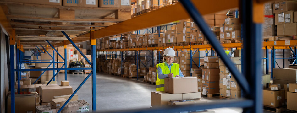 Senior woman working in warehouse, wearing reflective vest.