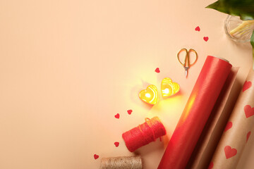 Romantic gift wrapping supplies on beige background. Red paper, heart candles, ribbon, and scissors with copy space.