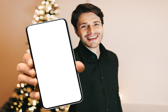Portrait of handsome smiling bearded young man in black shirt reaching hand to camera, trying to touch or grab something, staying at home, blurred background, selective focus