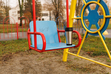 A swing set shows an empty seat with a coffee cup placed on it at a playground in the morning