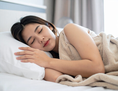 A beautiful young brunette woman with a calm smile is lying on a pillow in her bedroom, enjoying a morning of relaxation and healthy sleep at home