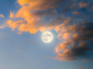 Full moon in the sky at sunset. Bright moon on a blue background between clouds. Celestial landscape.