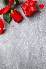 Vertical view of beautiful red rose, gift box and hearts on gray background