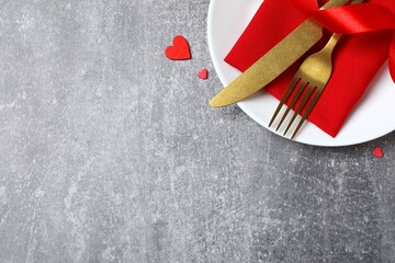 Top view of cutlery with a napkin, plate, and decorative hearts on a gray table with space for text. Valentine's Day romantic dinner