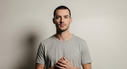 Fototapeta premium Serious man in gray t-shirt with hands clasped in front of a white background.